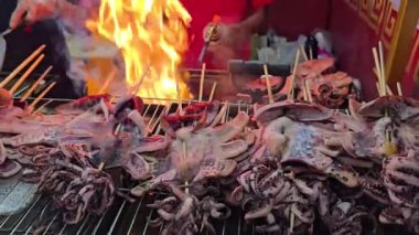 Aşçı mürekkep balığını meşale kullanarak açık bir ateşin üzerinde ızgara yaparak canlı bir sokak yemeği olan Tayland marketinin canlı atmosferini parlak alevler ve taze hazırlanmış deniz ürünleri ile yakıyor..