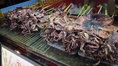 Asya 'daki bir yemek pazarında sunulan şiş kebap üzerinde taze ızgara kalamarlı canlı mutfak gelenekleri sergileniyor. Çokluortam içeriği için iyidir