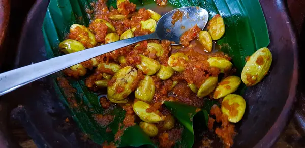 Muz yaprakları üzerinde servis edilen canlı bir tabak petai fasulyesi ve lezzetli kırmızı biber sosu. Otantik Güneydoğu Asya aşçılık gelenekleri ve Sambal Petai adlı cesur yemeğin altı çizildi