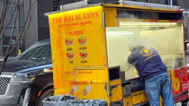 New York sokak satıcısı şehrin kaldırımında canlı sarı bir helal gıda arabasında taze yemek pişiriyor. Kalabalık bir çevresi ve yakınındaki park edilmiş arabalarla sokak yemekleri kültürünün somut örneğini veriyor. Çokluortam içeriği için iyi