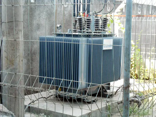 Yüksek voltajlı Transformatör, endüstriyel altyapı ve güvenlik ölçüsünü vurgulayarak endüstriyel bir ortamda güvenli bir çitle korunan yüksek voltajlı elektrik trafosunu tasvir eden bir görüntü.