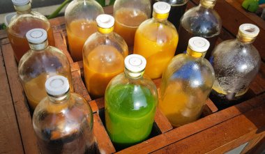 Yerel olarak Jamu adı verilen renkli doğal tıp şişeleri, güneşli bir günde ahşap kutuda sergileniyor, güneş ışığı altında ahşap bir kapta sergilenen sıvılarla dolu çeşitli renkli şişeler..