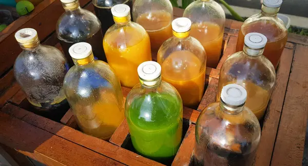 Yerel olarak Jamu adı verilen renkli doğal tıp şişeleri, güneşli bir günde ahşap kutuda sergileniyor, güneş ışığı altında ahşap bir kapta sergilenen sıvılarla dolu çeşitli renkli şişeler..