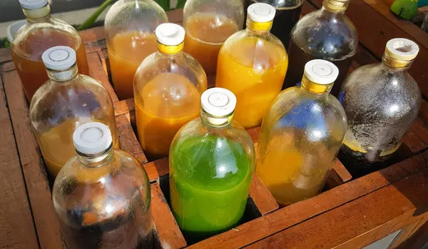 Yerel olarak Jamu adı verilen renkli doğal tıp şişeleri, güneşli bir günde ahşap kutuda sergileniyor, güneş ışığı altında ahşap bir kapta sergilenen sıvılarla dolu çeşitli renkli şişeler..