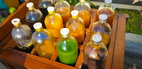 Yerel olarak Jamu adı verilen renkli doğal tıp şişeleri, güneşli bir günde ahşap kutuda sergileniyor, güneş ışığı altında ahşap bir kapta sergilenen sıvılarla dolu çeşitli renkli şişeler..