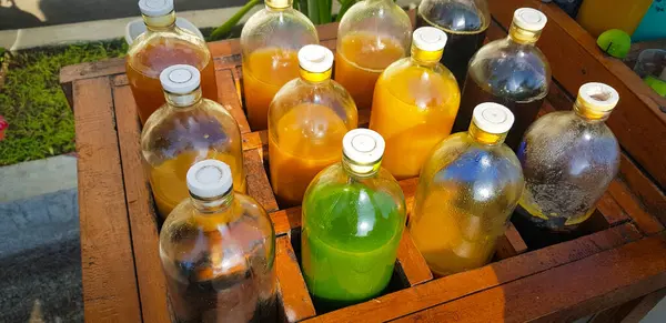 Yerel olarak Jamu adı verilen renkli doğal tıp şişeleri, güneşli bir günde ahşap kutuda sergileniyor, güneş ışığı altında ahşap bir kapta sergilenen sıvılarla dolu çeşitli renkli şişeler..