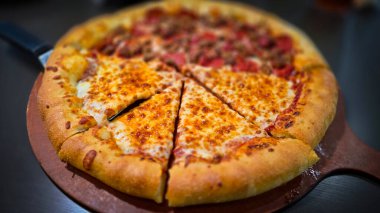 Tahta bir tahtanın üzerinde servis edilen peynirle et severlerin karışımından oluşan lezzetli bir pizza. Doldurulmuş altın peynir ve erimiş peynir taze ve karşı konulmaz lezzetleri vurgular ve ağız sulandırıcı bir mutfak deneyimi yaratır..