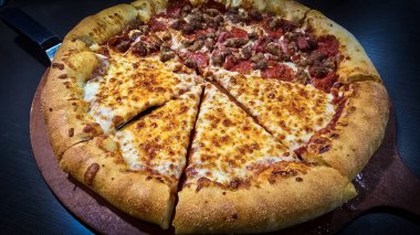Tahta bir tahtanın üzerinde servis edilen peynirle et severlerin karışımından oluşan lezzetli bir pizza. Doldurulmuş altın peynir ve erimiş peynir taze ve karşı konulmaz lezzetleri vurgular ve ağız sulandırıcı bir mutfak deneyimi yaratır..