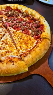 Tahta bir tahtanın üzerinde servis edilen peynirle et severlerin karışımından oluşan lezzetli bir pizza. Doldurulmuş altın peynir ve erimiş peynir taze ve karşı konulmaz lezzetleri vurgular ve ağız sulandırıcı bir mutfak deneyimi yaratır..