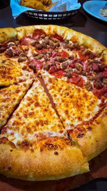 Tahta bir tahtanın üzerinde servis edilen peynirle et severlerin karışımından oluşan lezzetli bir pizza. Doldurulmuş altın peynir ve erimiş peynir taze ve karşı konulmaz lezzetleri vurgular ve ağız sulandırıcı bir mutfak deneyimi yaratır..