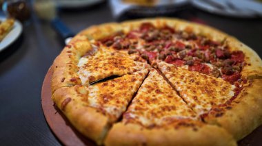 Tahta bir tahtanın üzerinde servis edilen peynirle et severlerin karışımından oluşan lezzetli bir pizza. Doldurulmuş altın peynir ve erimiş peynir taze ve karşı konulmaz lezzetleri vurgular ve ağız sulandırıcı bir mutfak deneyimi yaratır..