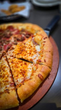 Tahta bir tahtanın üzerinde servis edilen peynirle et severlerin karışımından oluşan lezzetli bir pizza. Doldurulmuş altın peynir ve erimiş peynir taze ve karşı konulmaz lezzetleri vurgular ve ağız sulandırıcı bir mutfak deneyimi yaratır..