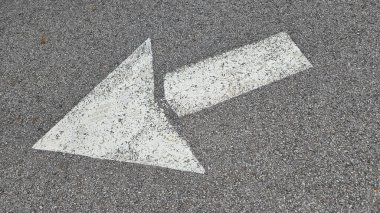 Asfalt yol yüzeyinde beyaz boyalı ok, ulaşım koşullarında yön ve navigasyonu temsil eder.