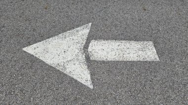 Asfalt yol yüzeyinde beyaz boyalı ok, ulaşım koşullarında yön ve navigasyonu temsil eder.