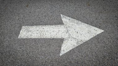 Asfalt yol yüzeyinde beyaz boyalı ok, ulaşım koşullarında yön ve navigasyonu temsil eder.