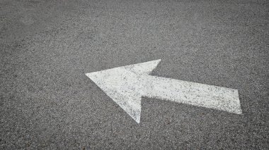 Asfalt yol yüzeyinde beyaz boyalı ok, ulaşım koşullarında yön ve navigasyonu temsil eder.