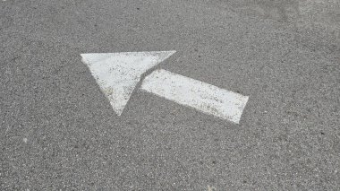 Asfalt yol yüzeyinde beyaz boyalı ok, ulaşım koşullarında yön ve navigasyonu temsil eder.