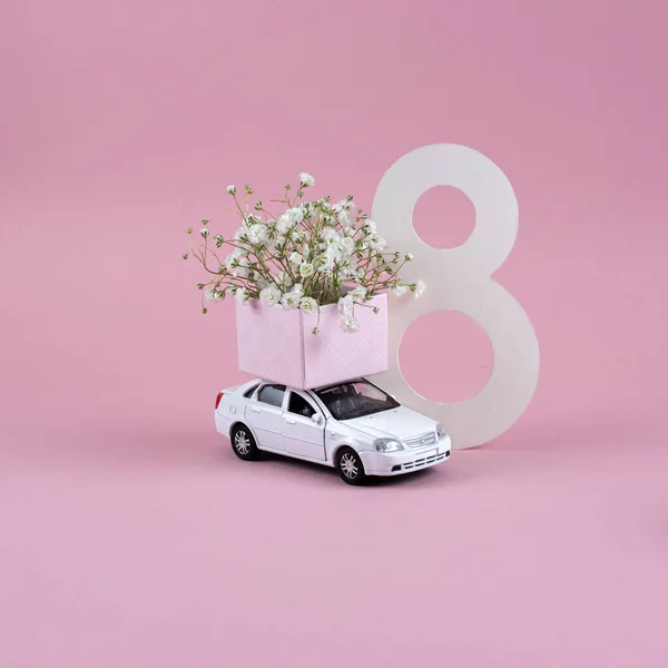 box of flowers on car on pink background. Holiday postcard with white toy car