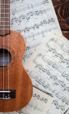Ukulele gitarı ahşap arka planda müzik sayfalarında yakın planda.