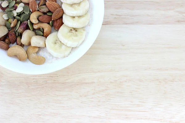 Overnight oatmeal with mixed nut and banana in the white bowl on the table