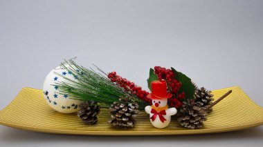 Yeni yıl kompozisyonu. Koniler, dekoratif viburnum dalı, bir Noel ağacı oyuncağı bir kardan adam ve bir top dikdörtgen kıvrımlı bir tabakta düzenlenir.