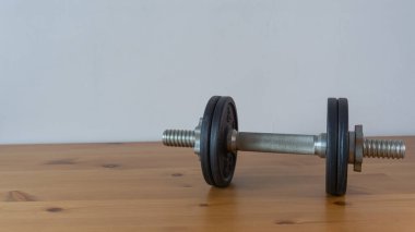 Siyah dambıl, gümüş tutuş, yansıtıcı ahşap yüzey, minimalist spor aletleri.