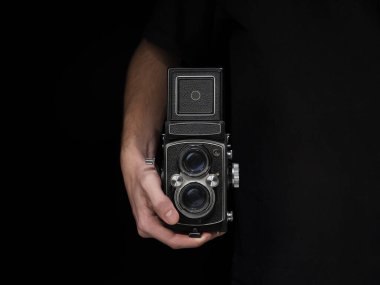 İzole edilmiş siyah bir arkaplanda eski bir analog kamera tutan bir kişi..