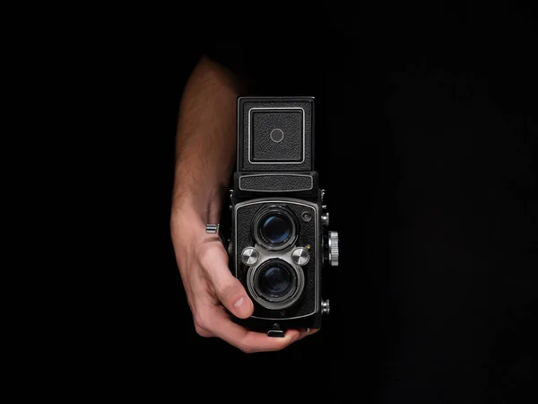 A person holding an old analog camera on an isolated black background.
