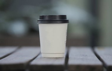 yakın planda, ahşap bir masada, bulanık bir arka planda, bir bardakta kahve.