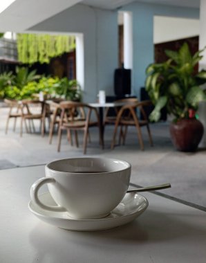 Ahşap bir masanın üzerinde masa ve sandalyelerin bulanık arkaplanlı bir fincan çay.