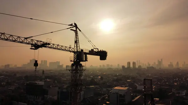 Jakarta, Endonezya - 16 Ekim 2024: Sanayi inşaat vincinin silüeti kentsel arka plan ve sabah güneş ışığı