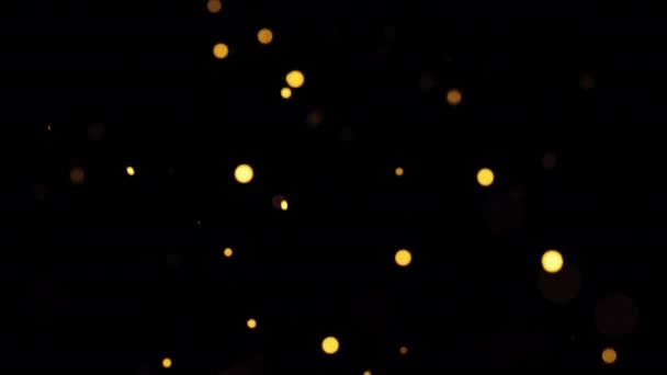 美しいループアニメーションは黒い抽象的な背景に浮かぶ金のオレンジ色のボケ粒子を光らせます 冬のクリスマスのための4Kの継ぎ目が無いループ新しい年テーマの背景 — ストック動画