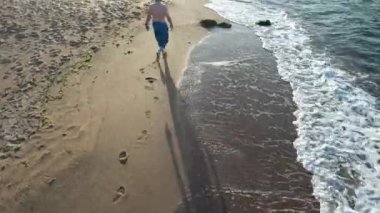 Kumsalda yürüyen, plajda gün batımında yürüyen bir adam.