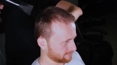 Berber, saç kurutma makinesiyle kızıl saçlı bir adamın saçını kurutuyor.