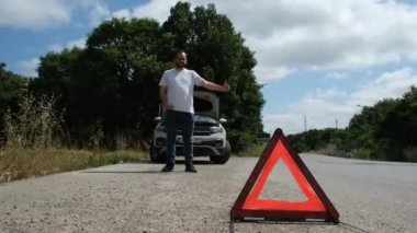 Bozuk arabasının yanında yardım isteyen bir adam otostop çekerken yardım istiyor.