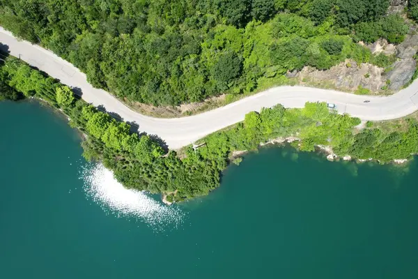 Göl kenarındaki orman yolu ve güneş yansıması.
