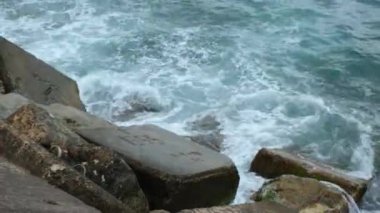 Dalgalar, deniz kenarındaki kayalara vuran beyaz köpük dalgaları. 