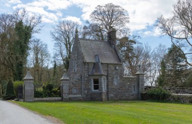 Koyu pencereli gri taş bir bina ve taştan yapılmış gri çit direkleri.