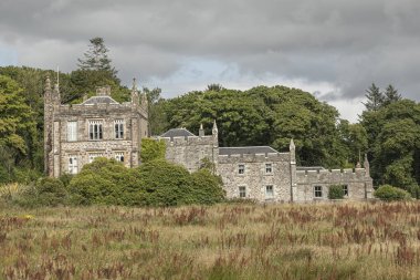 Gri fırtınalı gökyüzüne karşı eski bir İskoç binasında kuru bir çimen tarlasına bakıyorum.