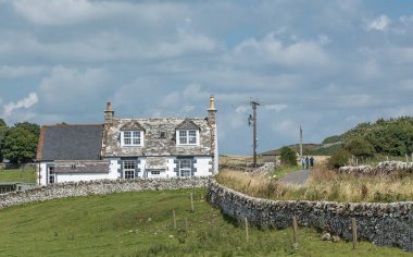 İskoç kulübesi, liken kaplı duvarları, çatısı, patikası ve yürüyüşçüleri olan