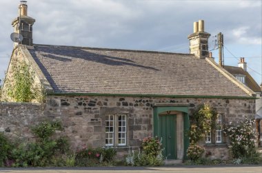 Korunaklı ön kapının etrafındaki güller yeşile boyanmış İskoç kulübesi.