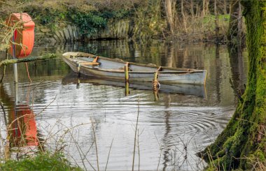 Eski tekne bataklığın ortasına bağlanmış ve yakınlardaki bir direkte can simidi var.