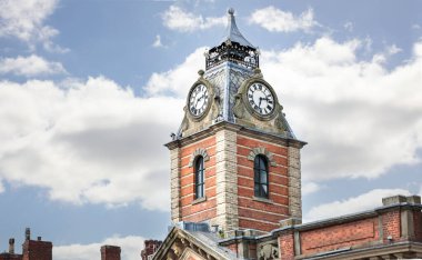 Mavi bulutlu gökyüzüne karşı kırmızı tuğladan yapılmış etkileyici bir saat kulesi.