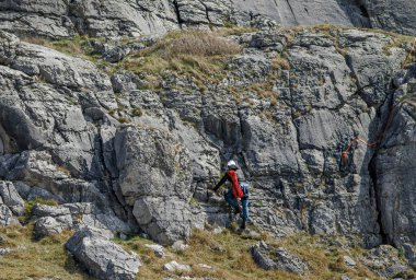 Kireçtaşı bir yamaçta tırmanmaya başlayan kırmızı bir ip taşıyan dağcı.