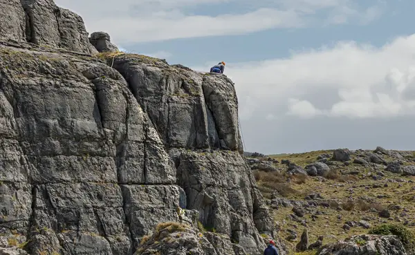 stock image Climber wearing a red helmet sat on the edge of a rock with another climber at the bottom