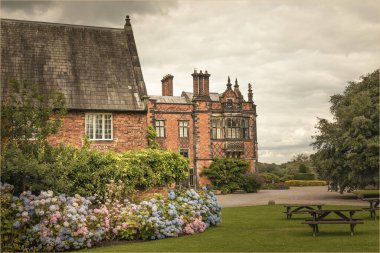 Gardens with borders of flowers and benches surrounding a stately home clipart