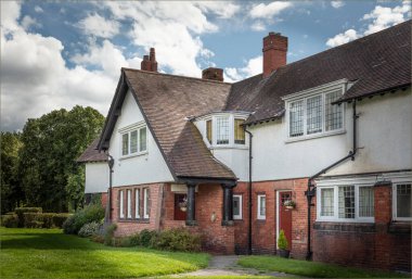 Port Sunlight, Wirral, İngiltere - 26 Temmuz 2024 - Çatısı koyu pencere ve iki kırmızı ön kapısı olan eski tip vintage mülk