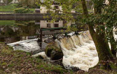 Uzerche, Coreze, Nouvelle-Aquataine, Fransa - 8 Kasım 2024 - Nehrin karşısındaki küçük tarihi Roma kasabasında, suda yansımaları olan Weir
