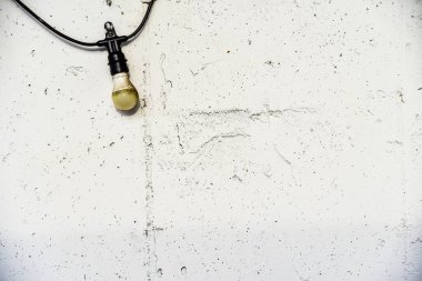 Zincirden bir ampul sarkıyor. Zincir bir duvara bağlı. Ampul beyaz ve yeşil bir tabanı var.