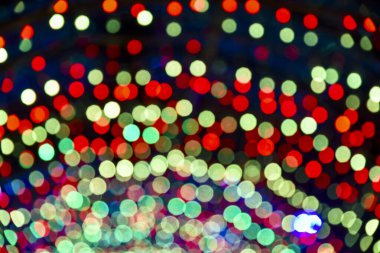 Yeşil, kırmızı ve mavi ışıkları olan bir Noel ağacının bulanık görüntüsü. Işıklar ağacın her tarafına saçılmış, neşeli bir atmosfer yaratıyor.